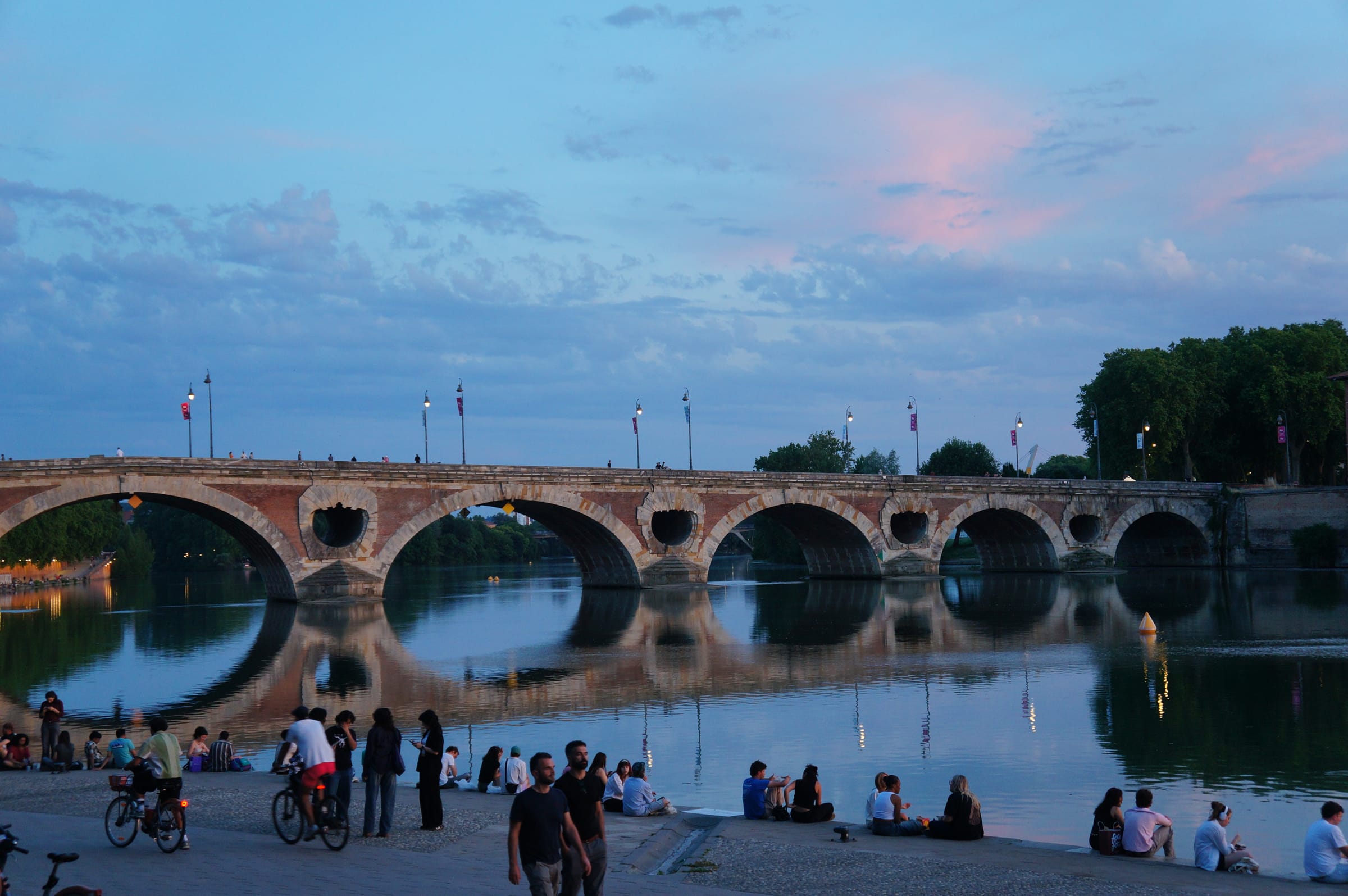 Pont Neuf over la Garonne i skumringen, med folk samlet langs elvebredden i Toulouse